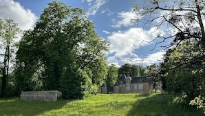 Ein großes, historisches Gebäude mit mehreren Türmen und einer Steinmauer, umgeben von üppiger Vegetation und Bäumen.