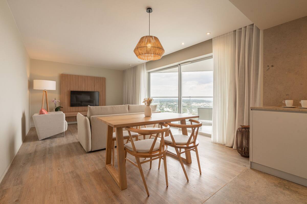 Ein modernes Wohnzimmer mit einem Holzesstisch, zwei Stühlen, einer Couch und einem Fernseher.