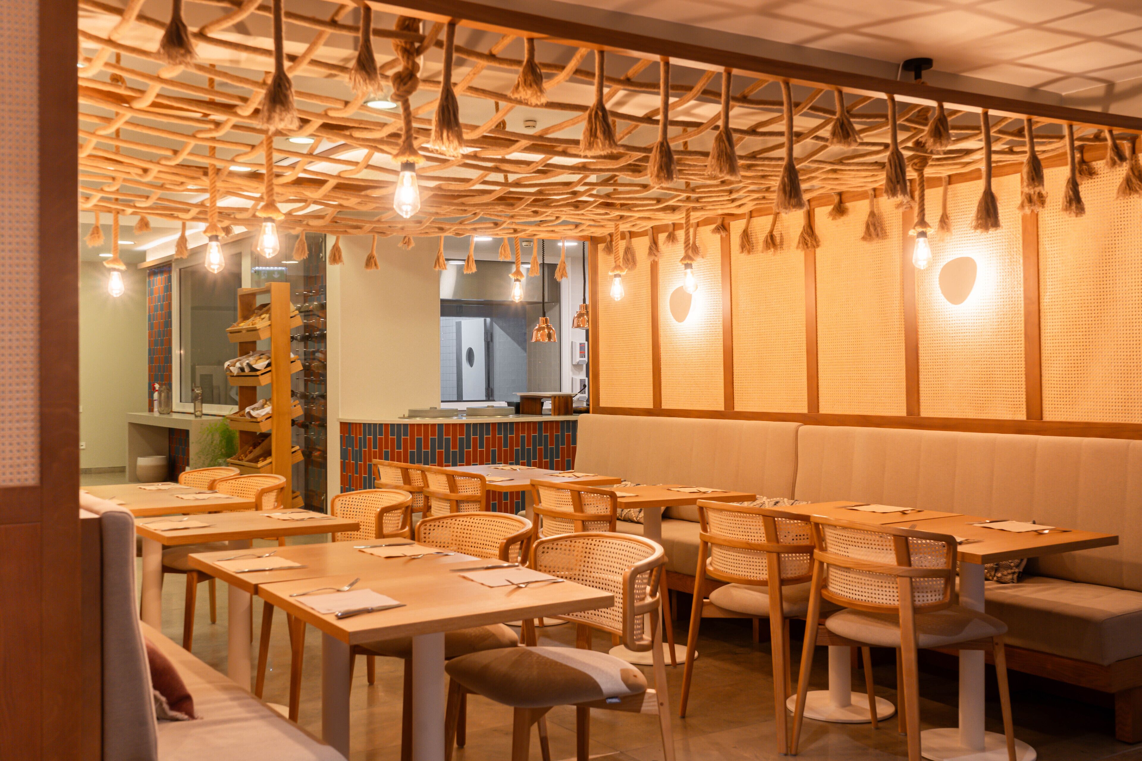 Interior de restaurante con mesas y sillas de madera, una barra y un área de estar con un banco acolchado.