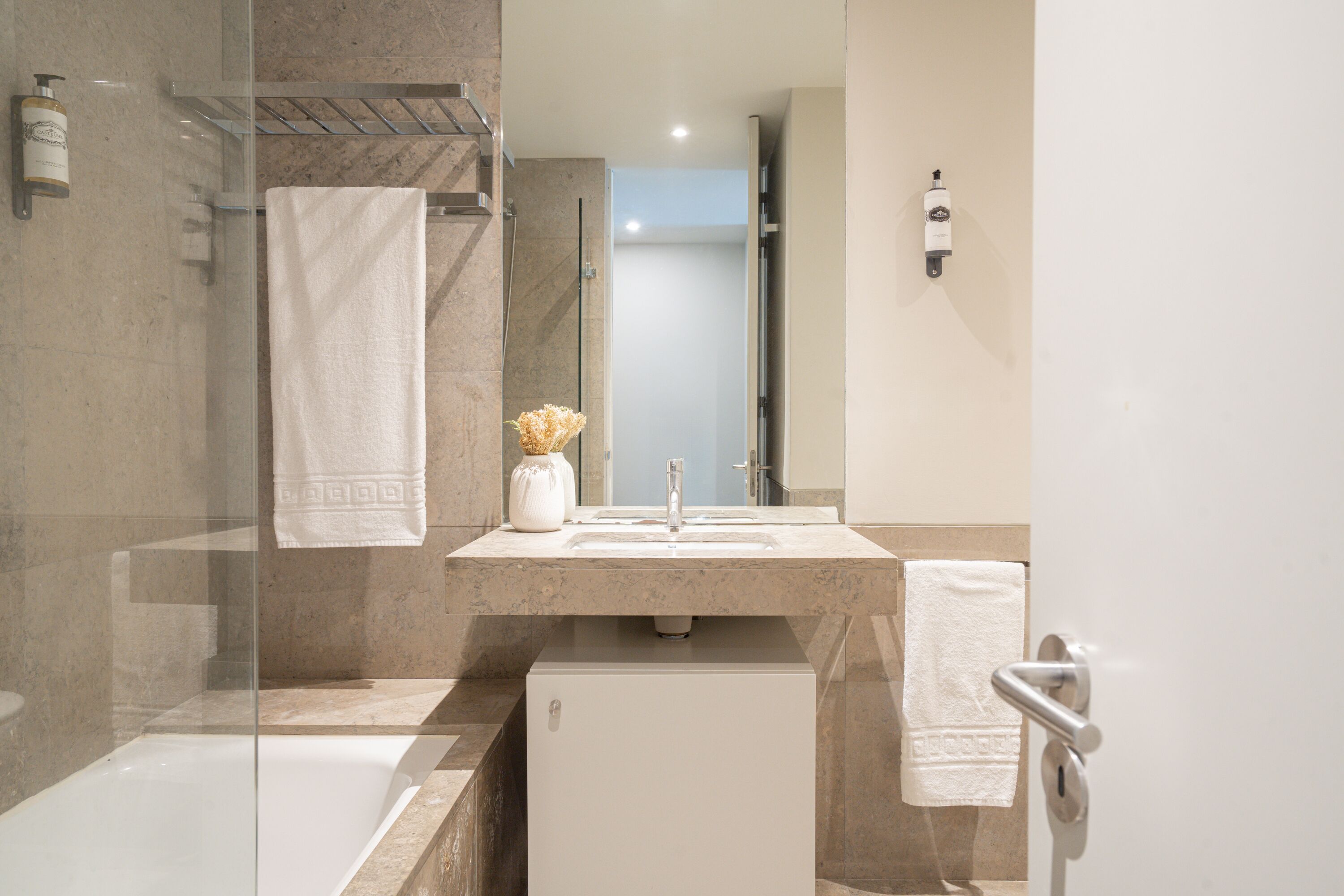 Un baño moderno con ducha de vidrio, lavamanos blanco y un mueble blanco pequeño.
