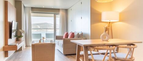 Una sala de estar moderna con un sofá, una mesa de comedor con sillas, un televisor montado en la pared y un ventanal con vistas.