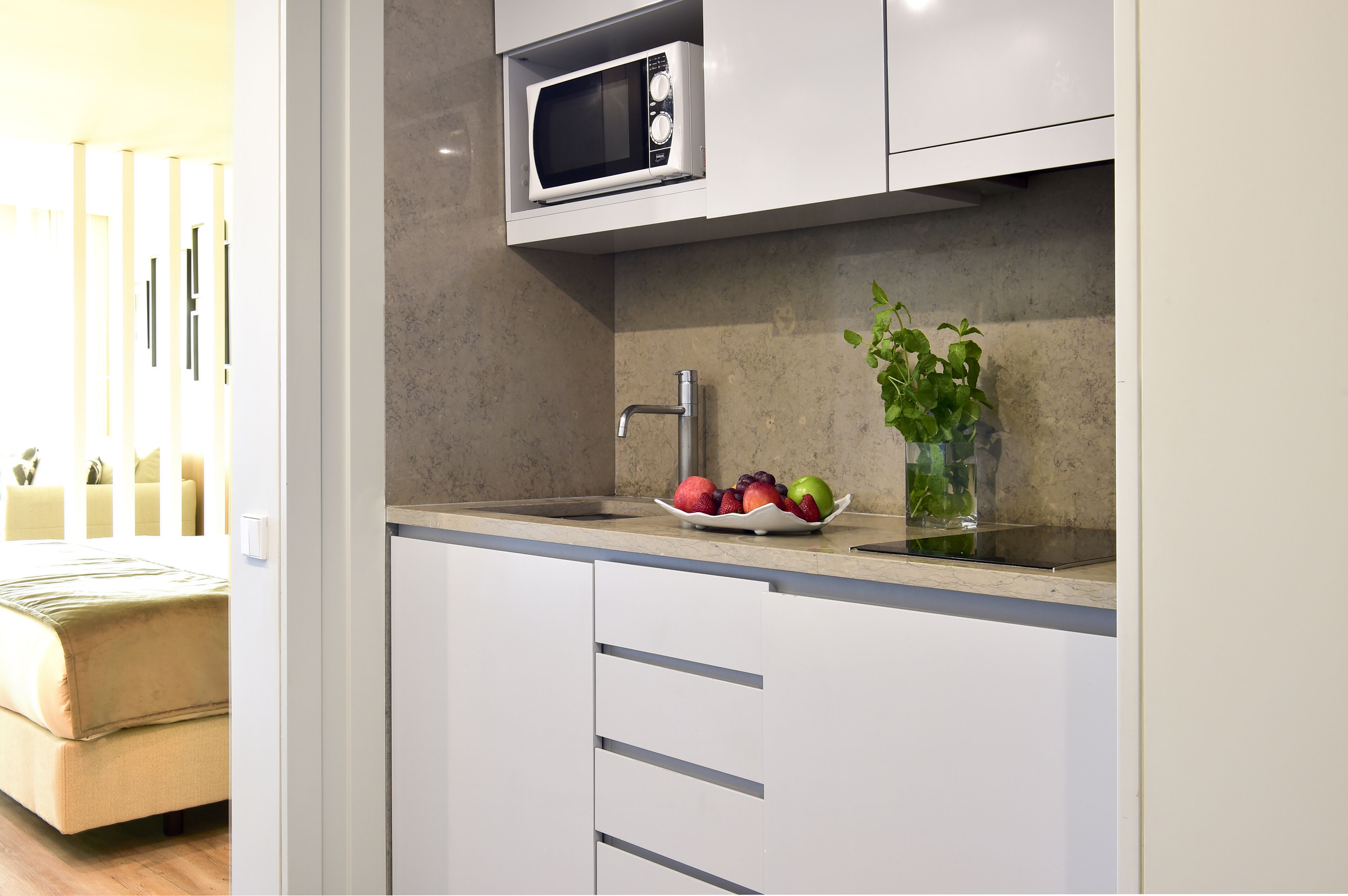 A modern kitchen with white cabinets, a microwave, a fruit bowl, and a potted plant.