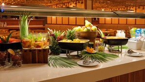 Un buffet proposant une variété de fruits, un saladier rempli d’ananas et un verre de jus.