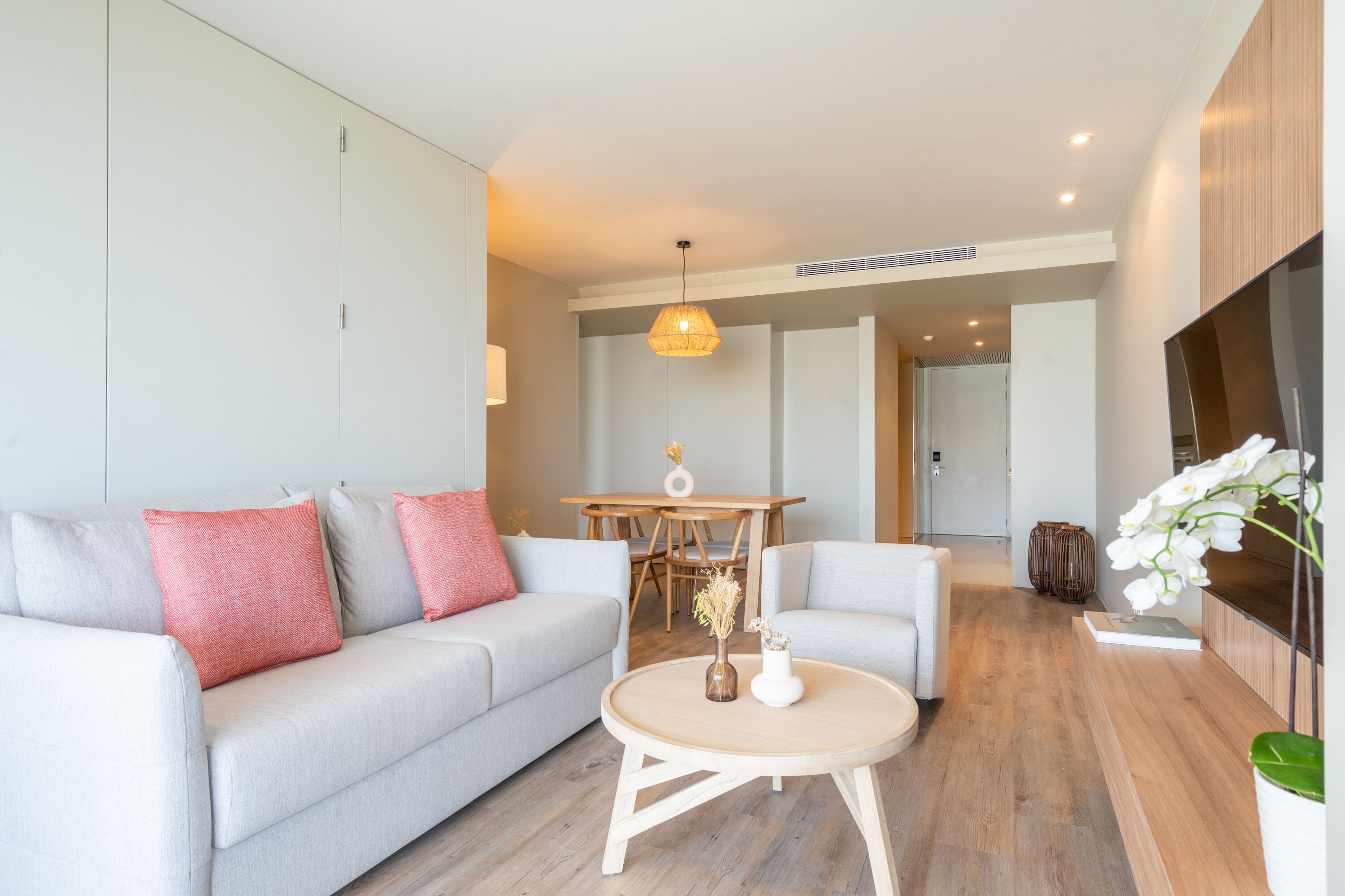 Een moderne woonkamer met een grijze bank, een ronde salontafel, en een eethoek op de achtergrond.