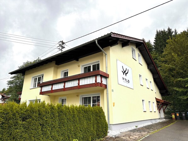 A two-story building with a yellow facade, a balcony with wooden railings, and a sign indicating it is an apartment complex.