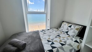 Et soveværelse med en seng, et vindue der viser udsigt over stranden og et håndklæde på sengen.