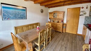 Een houten eettafel met stoelen, een houten bank, een keuken met houten keukenkastjes en een houten plafond.