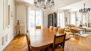 A spacious dining area with a large wooden table and chairs, a chandelier, and a view of the city through large windows. - Timeless Majesty, by Veeve (Paris)