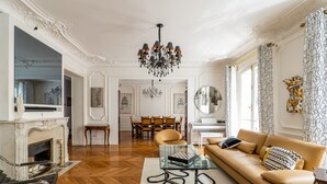 A spacious living room with a fireplace, a sofa, a glass coffee table, and a chandelier. - Timeless Majesty, by Veeve (Paris)
