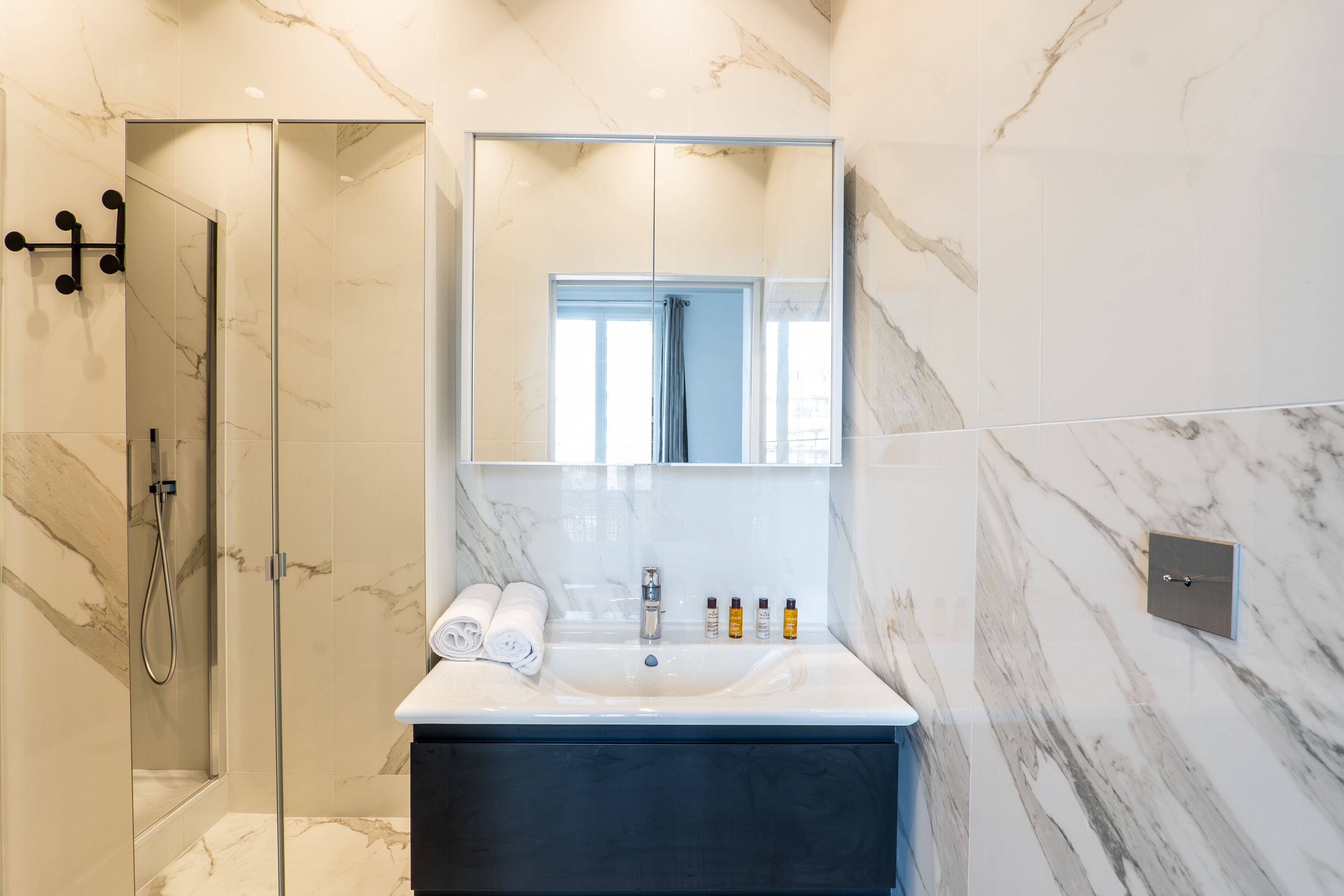 A modern bathroom with a glass shower enclosure, a large mirror, a white sink with a dark vanity, and a marble backsplash.