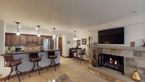 A modern kitchen with a bar area, a fireplace, and a flat-screen TV mounted above it. - Lionshead Village - Montaneros 1 Bedroom (Vail)