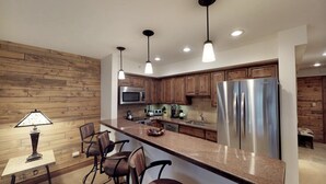 A modern kitchen with wooden cabinetry, stainless steel appliances, and pendant lighting. - Lionshead Village - Montaneros 1 Bedroom (Vail)