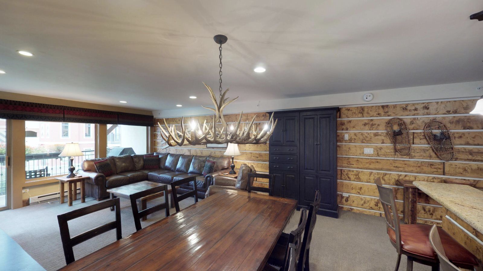 A spacious living area with a wooden dining table, leather sofa, and a modern chandelier.