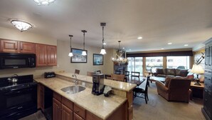 A modern kitchen with granite countertops, a built-in microwave, and a coffee maker. There is a dining area with a table and chairs, and a living room with a sofa and a lamp. - Upscale 2-bedroom Residence in Resort-style Setting With Saline Outdoor Pool, 2 hot Tubs (Vail)
