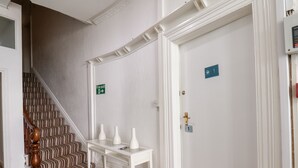 Ein Hotelgang mit Treppe, einem weißen Konsolentisch mit Vasen und einer Tür mit Nummernschild.