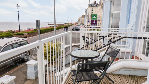 Ein Balkon mit Tisch und Stühlen mit Blick auf eine Straße, auf der Autos geparkt sind und Gebäude stehen.
