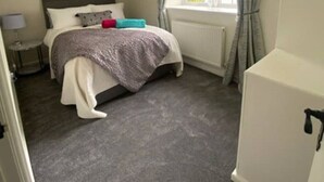 Ein Schlafzimmer mit einem Bett, einem Fenster mit Vorhängen, einem Heizkörper und einem kleinen Nachttisch.