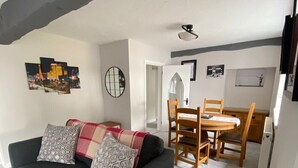 Ein Wohnzimmer mit einem dunkelgrauen Sofa, einem Esstisch mit Holzstühlen und einem Deckenventilator.