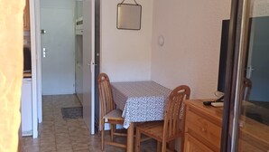 A small dining area with a table and chairs, a wooden cabinet, and a wall-mounted light fixture. - Appartement Avec la Piscine Privée (Cavalaire-sur-Mer)