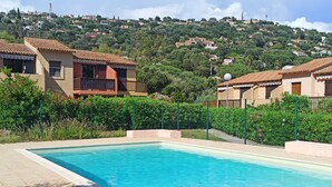 A swimming pool with a tiled deck, surrounded by a green fence and lush vegetation. - Appartement Avec la Piscine Privée (Cavalaire-sur-Mer)