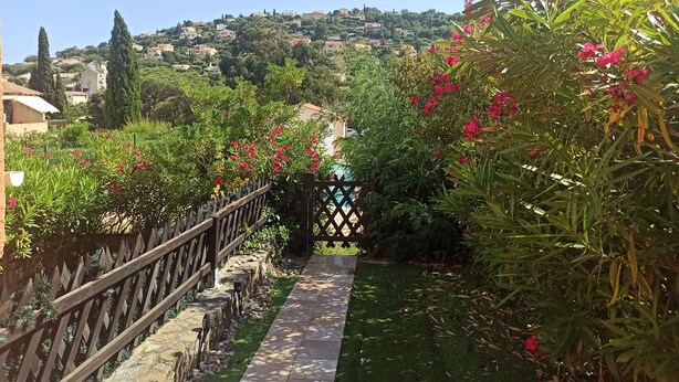A garden pathway with a wooden fence, green grass, and pink flowers. - Appartement Avec la Piscine Privée (Cavalaire-sur-Mer)