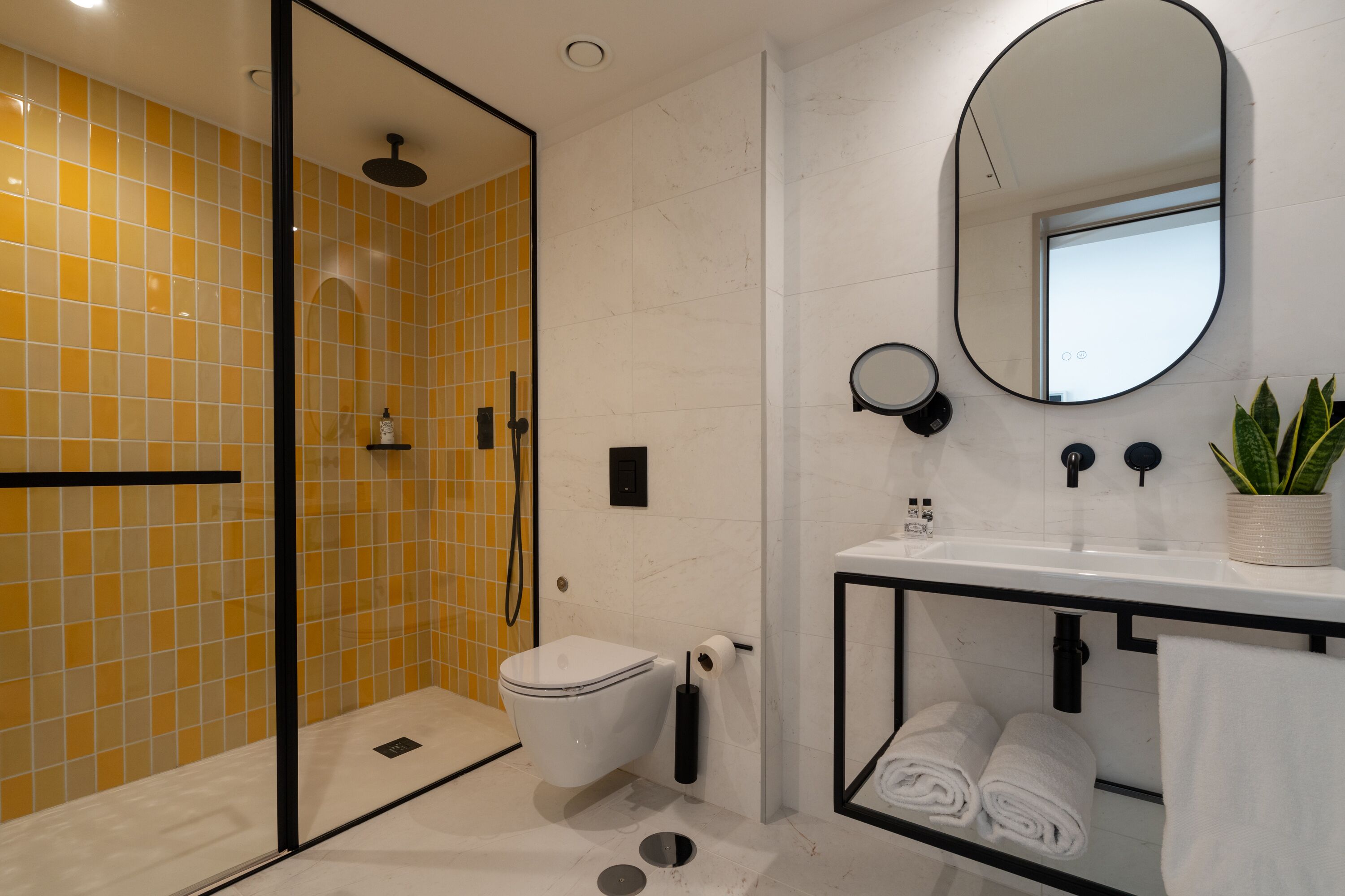 A modern bathroom with a glass shower enclosure, a toilet, a sink with a mirror, and neatly rolled towels.