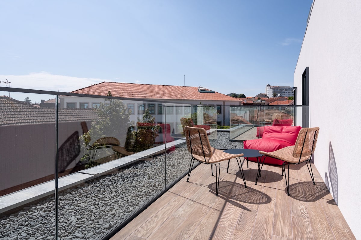 Terraza en la azotea con barandilla de cristal, mobiliario de mimbre y un sofá rojo.