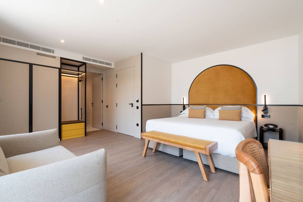 Una habitación de hotel moderna con una cama grande, un banco, un escritorio y una silla.