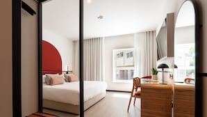 A modern hotel room with a bed, a desk, a chair, a mirror, and a window with curtains. - The Editory Garden Porto Hotel (Porto)