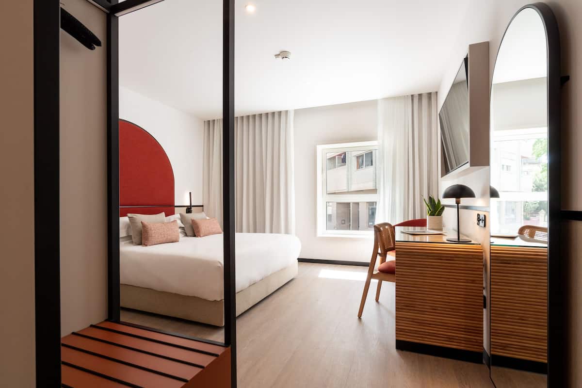 Una habitación de hotel moderna con cama, escritorio y un espejo grande.