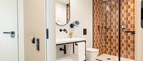 A modern bathroom with a glass shower enclosure, a white sink with a mirror, and a toilet.