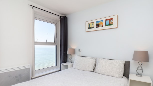 Une chambre à coucher avec un lit, deux tables de chevet, une fenêtre avec des rideaux et un tableau encadré au mur.