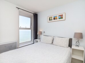 A bedroom with a bed, two bedside tables, a window with curtains, and a framed picture on the wall. - Fishermans Watch (Bridlington)