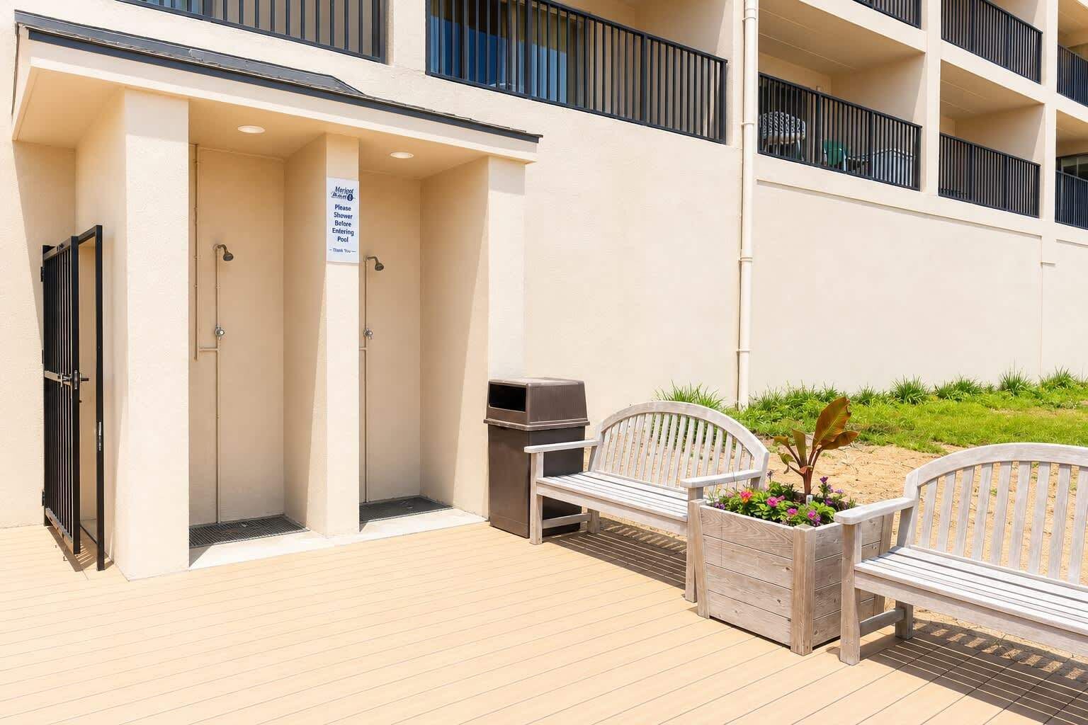 Un espace aménagé au bord de la piscine, avec un panneau indiquant qu’il faut prendre une douche avant d’entrer dans l’eau, un barbecue et deux bancs en bois.