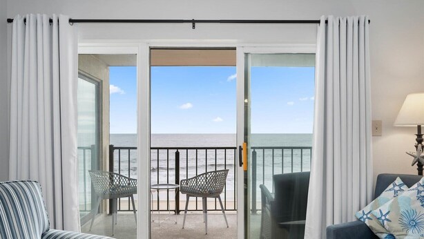 Une pièce avec un balcon, une table, deux chaises, un canapé et une lampe.