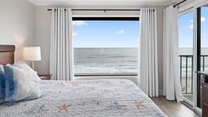 Une chambre à coucher avec un lit, une table de chevet, une lampe et une vue sur l’océan grâce à de grandes fenêtres.