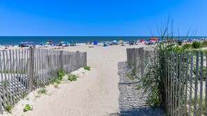 Une plage avec une clôture en bois, un sentier sablonneux et des parasols.