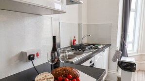 Cozinha com pão, tomates, uma garrafa e copos em cima do balcão.