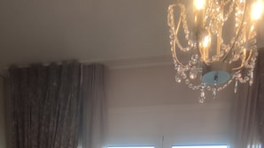 Une chambre d’hôtel avec un grand lit, un lustre, une vue sur la mer par une porte coulissante et un tapis à motifs.