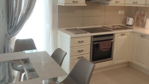 Une cuisine moderne avec des armoires blanches, un four encastré et un coin repas comprenant une table et des chaises en verre.