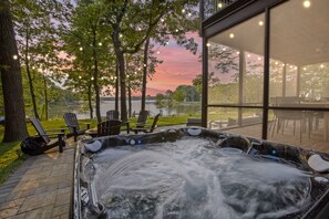 Un bain à remous avec vue sur un lac et le coucher de soleil, entouré de meubles de jardin et d’arbres.
