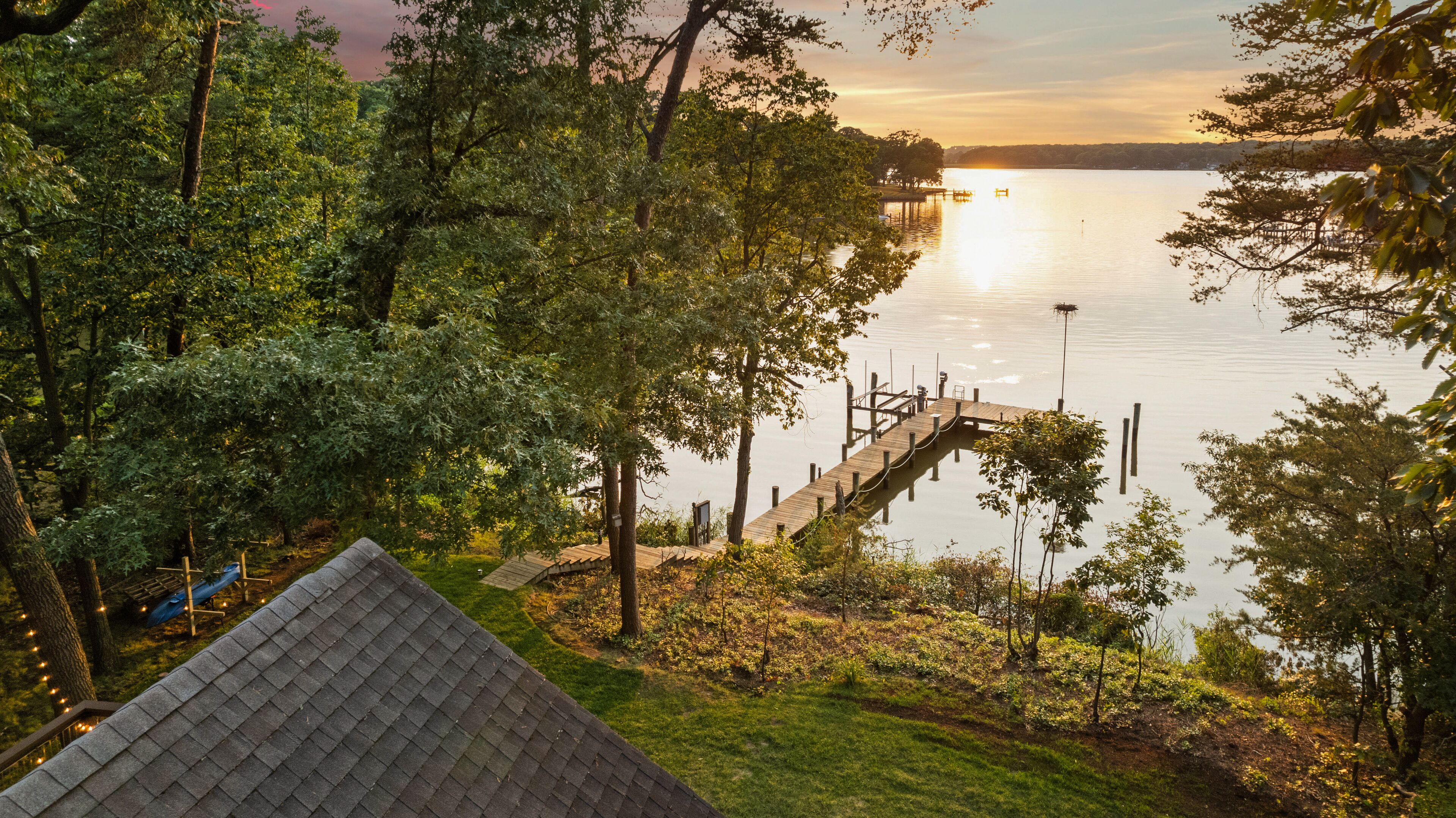 A lakeside property with a wooden dock extending into the water, surrounded by dense trees and a grassy area.
