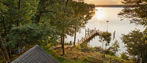 A lakeside property with a wooden dock extending into the water, surrounded by dense trees and a grassy area.