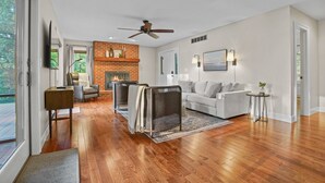 A spacious living room with hardwood flooring, a fireplace, a ceiling fan, a grey sofa, and a television mounted on the wall. - Harbor View Haven | Waterfront w/ Hot Tub + Dock! (Chestertown)