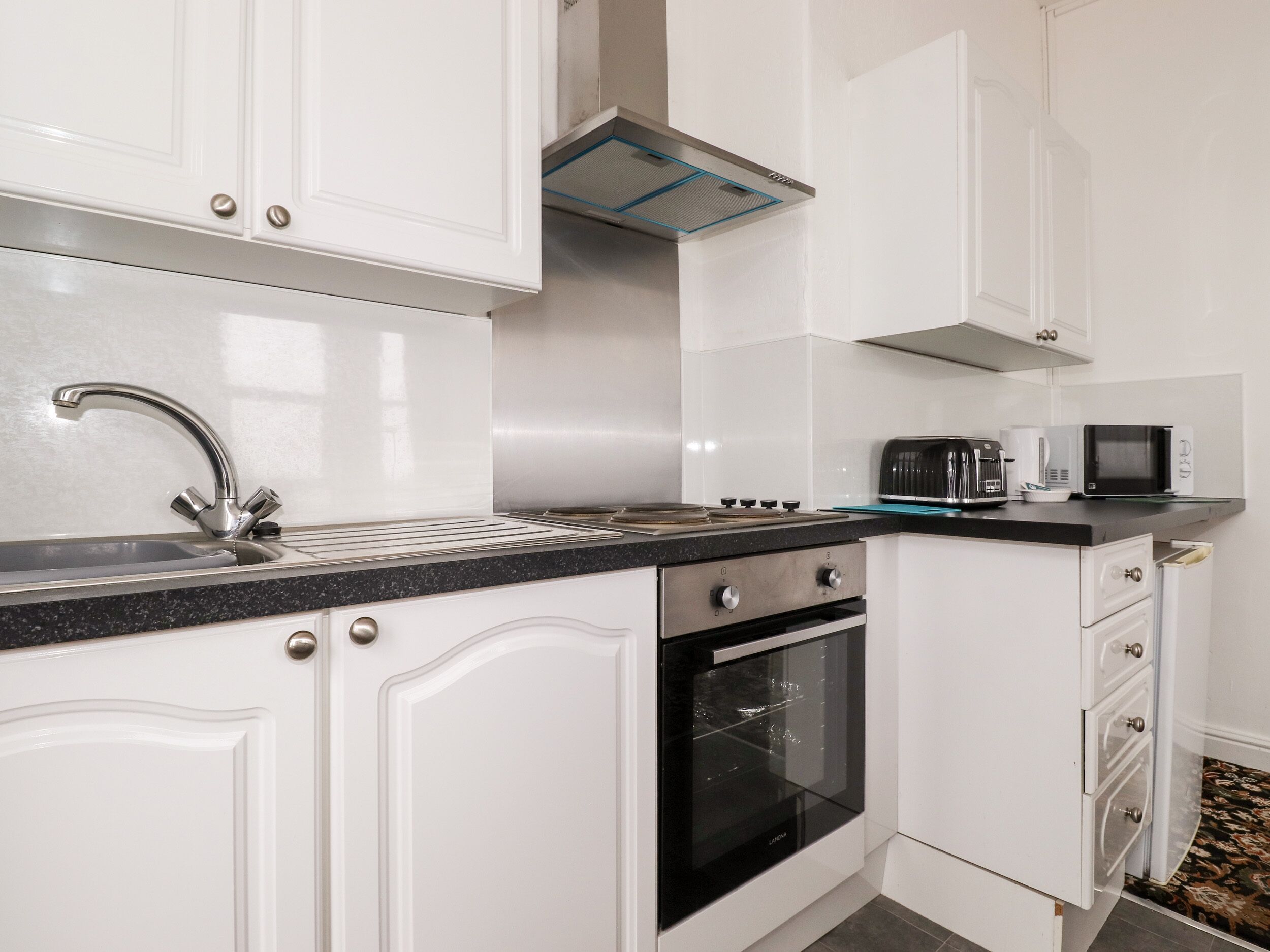 Una cocina moderna con armarios blancos, un lavamanos de acero inoxidable, un horno empotrado y un microondas en la encimera.
