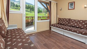 A room with a sofa, a window with a view of a green landscape, and a picture on the wall. - Ski-in/Ski-out apartment for 6 in Avoriaz with balcony and WiFi (Avoriaz)