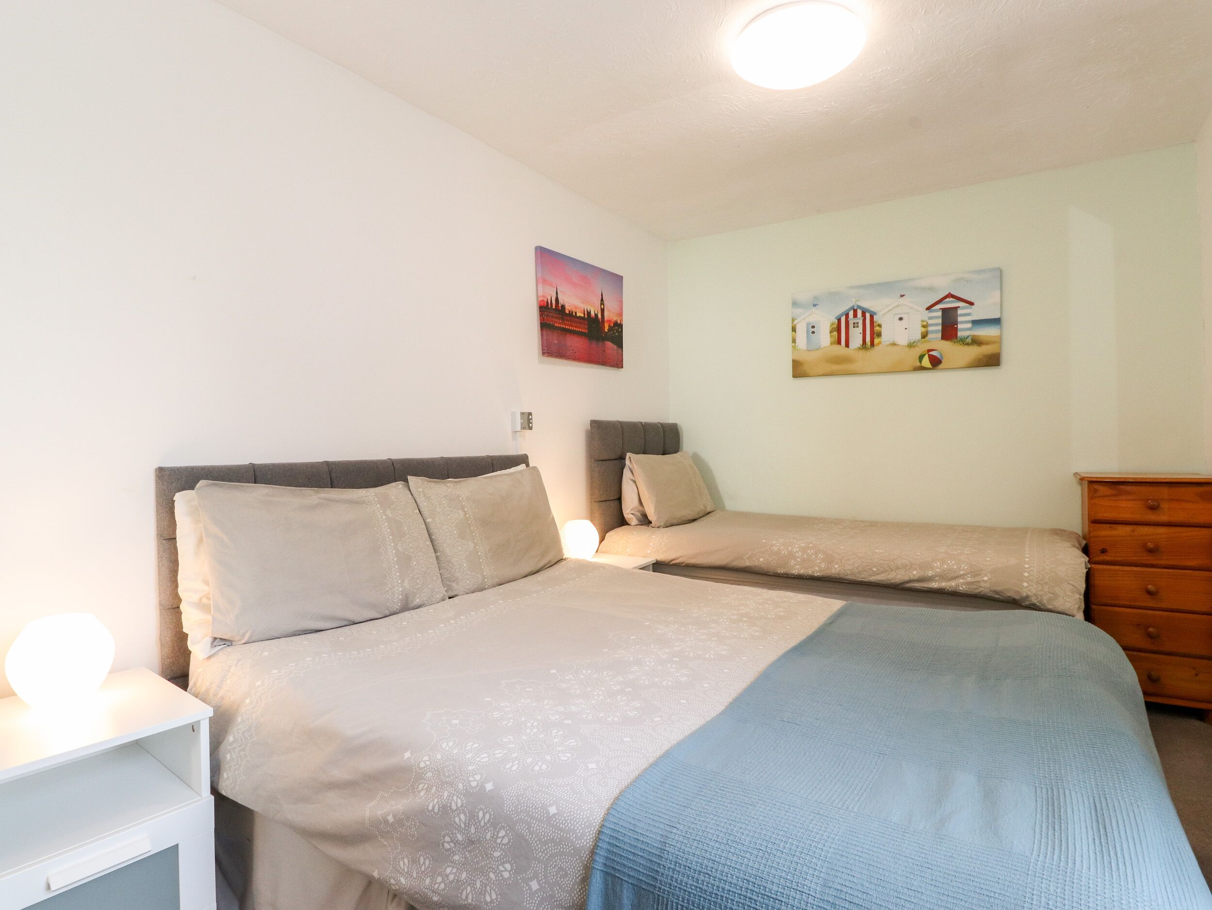 Ein Schlafzimmer mit zwei Betten, einem Nachttisch, einer Kommode und zwei Wandbildern.