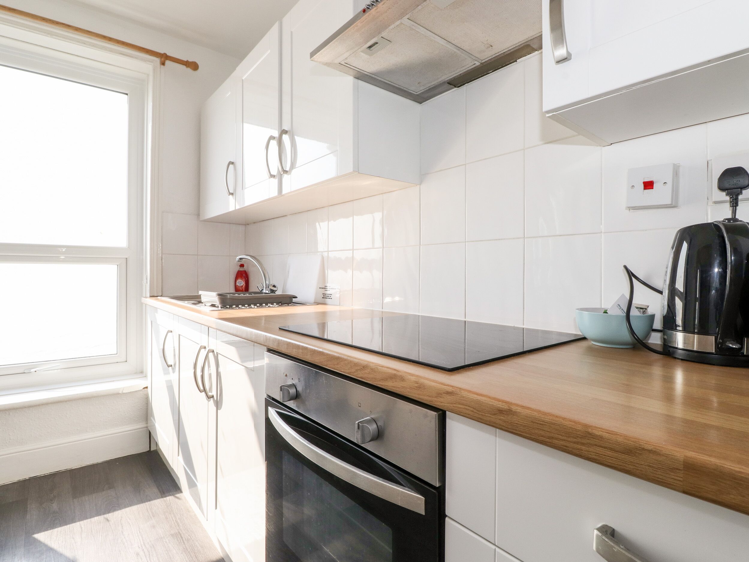 Una cucina moderna con mobili bianchi, un piano di lavoro in legno, forno integrato e bollitore.