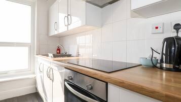 Una cucina moderna con mobili bianchi, un piano di lavoro in legno, forno integrato e bollitore.