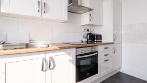 Una cocina moderna con armarios blancos, una campana extractora de acero inoxidable, una cafetera y un hervidor sobre la encimera.